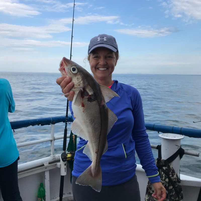 a woman holding a fish in front of a body of water