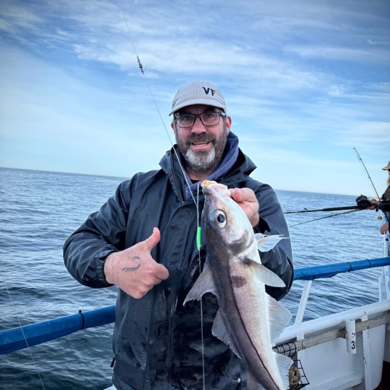 a man holding a fish on a boat in a body of water