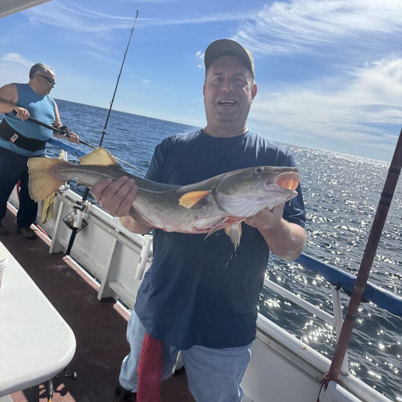 Man on a boat holding a large fish, with the ocean and sky in the background.