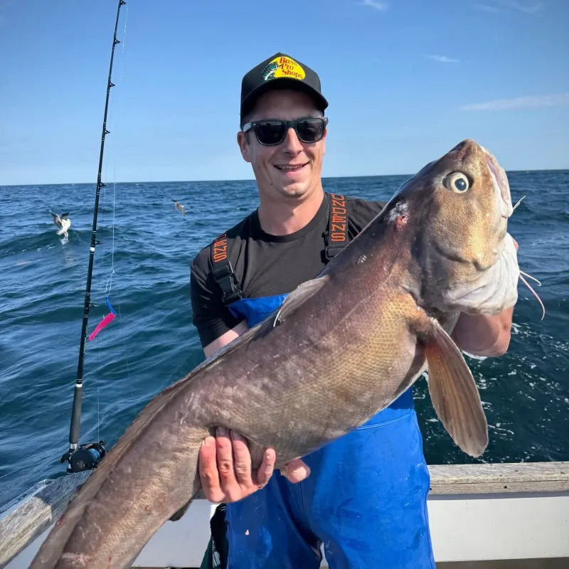 Man on boat holding large fish with fishing rod in background.