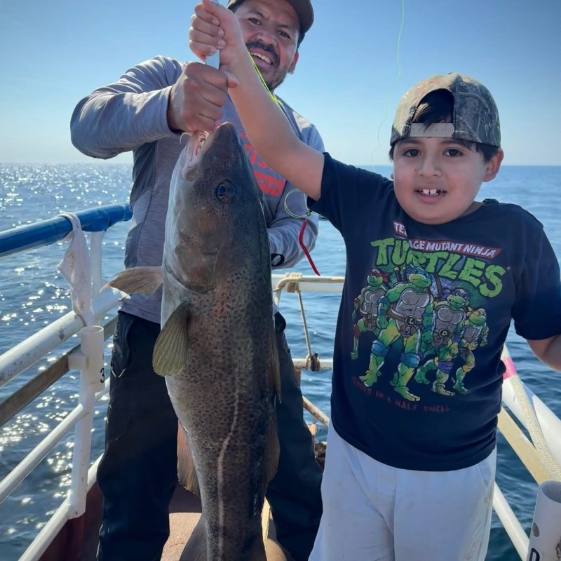 A man and child on a boat, smiling and holding a large fish together.