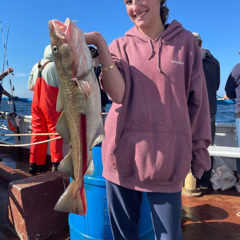 Smiling person holding a large fish on a boat with blue sky in background.