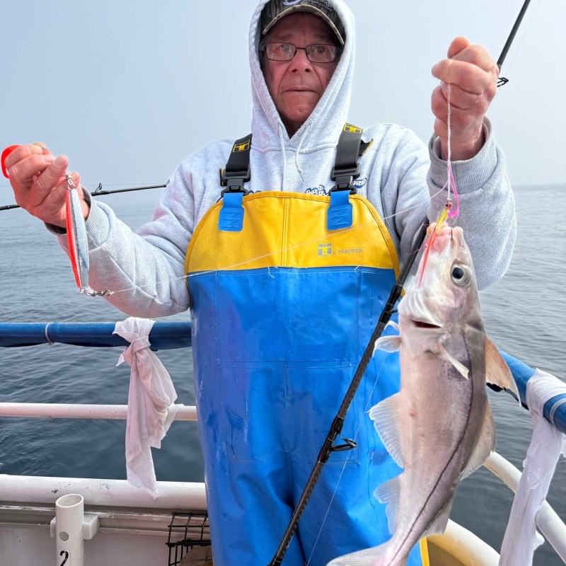 Person in blue-yellow overalls holding a fish on a boat.