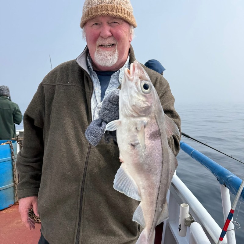 Man on boat holding a large fish, wearing a knit hat and jacket.