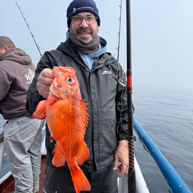 Man holding a bright orange fish on a boat with fishing rods.