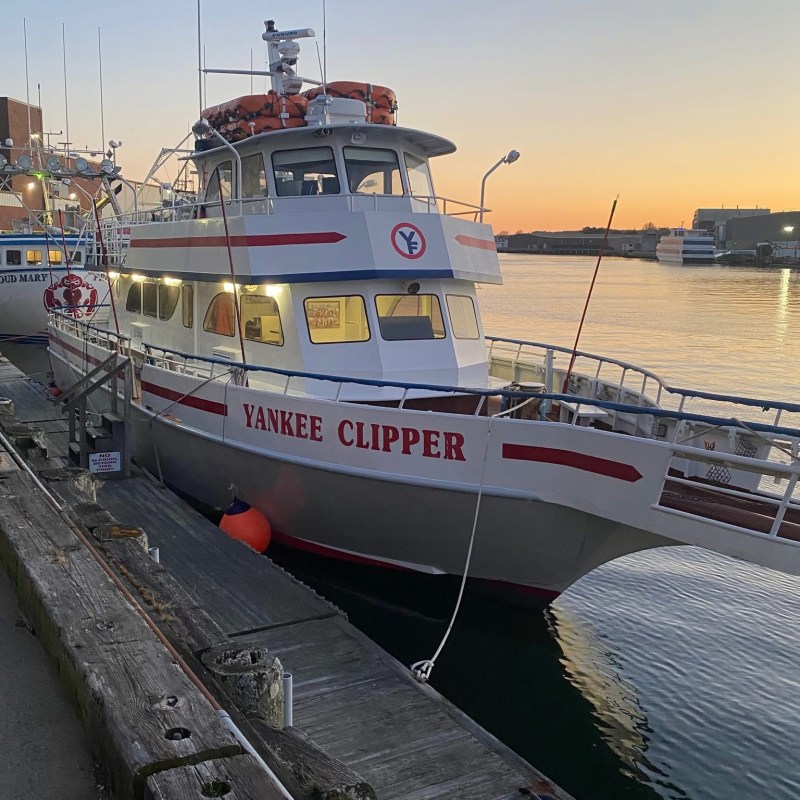 A boat named Yankee Clipper docked at sunrise on a calm river.