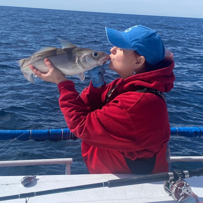 Person in red hoodie kissing a fish on a boat at sea.