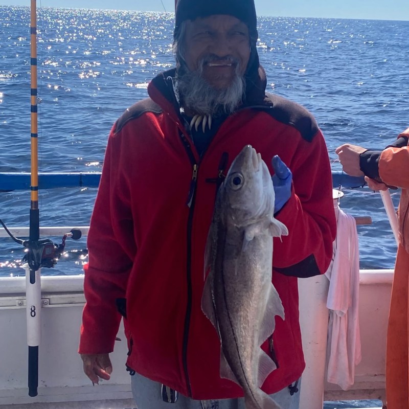 Person in red jacket holds a fish on a boat against a sunny ocean backdrop.