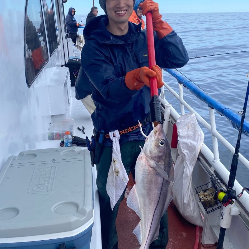 Fisherman on boat holding a large fish on a hook, smiling.