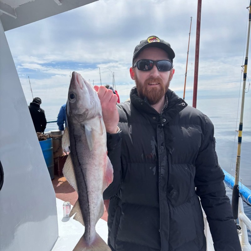 Person holding a fish on a boat, wearing a black jacket and sunglasses.