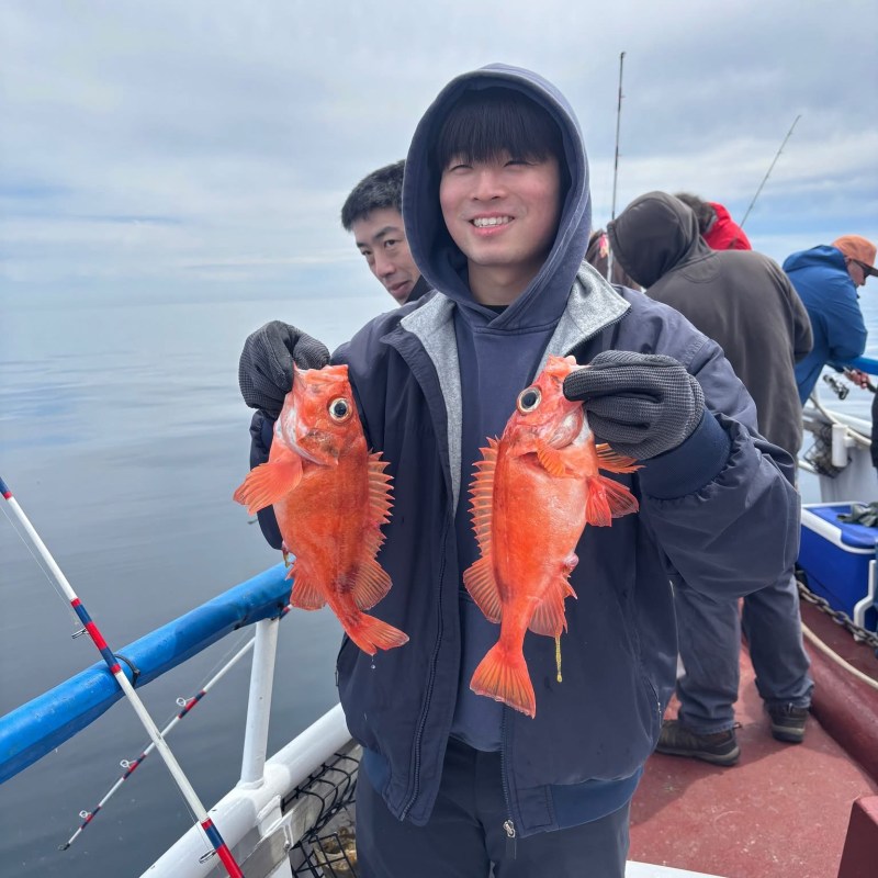 Person holding two orange fish on a boat with overcast sky.