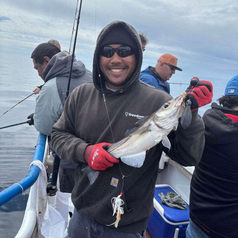 Smiling person on a boat holding a fish, surrounded by others fishing.