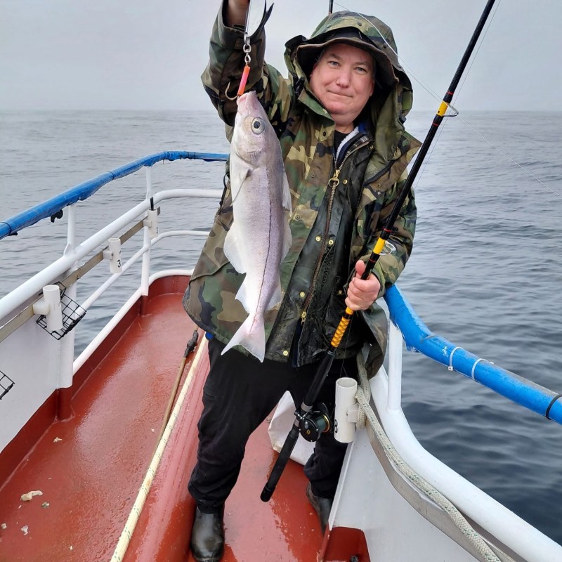 Person holding a fish on a boat in rainy weather.