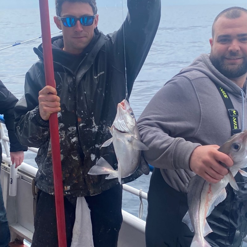Two men on a boat holding fish, with the ocean in the background.