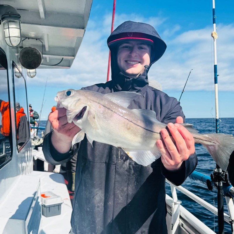 Person holding a fish on a boat, smiling, with ocean in the background.