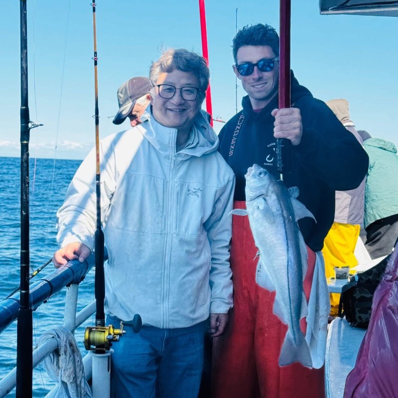 Two people on a boat holding a fish they caught, with fishing rods nearby.