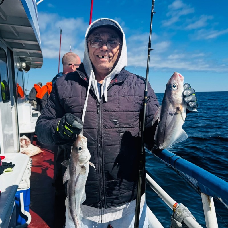 Person on boat holding two fish with ocean in background.
