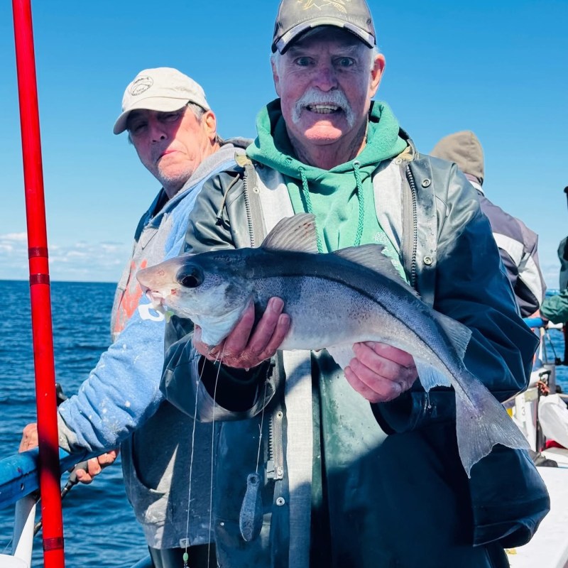 Two people on a boat holding a fish, ocean in the background.