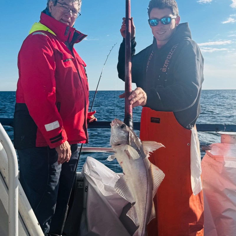 Two people on a boat holding a large fish with a rod.