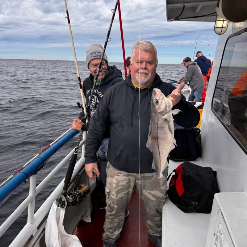Two people on a boat holding fishing rods with a caught fish.