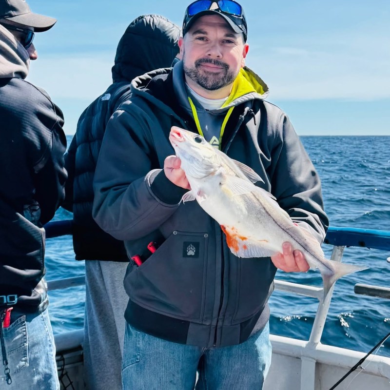 Man holding fish on boat with ocean background.