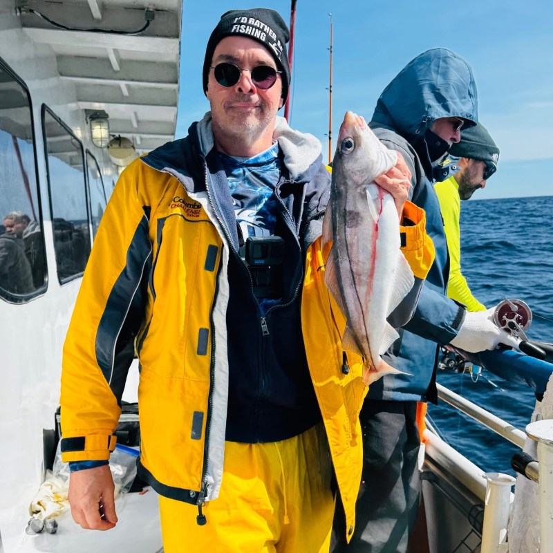 Person in yellow gear holding fish on a boat with ocean background.