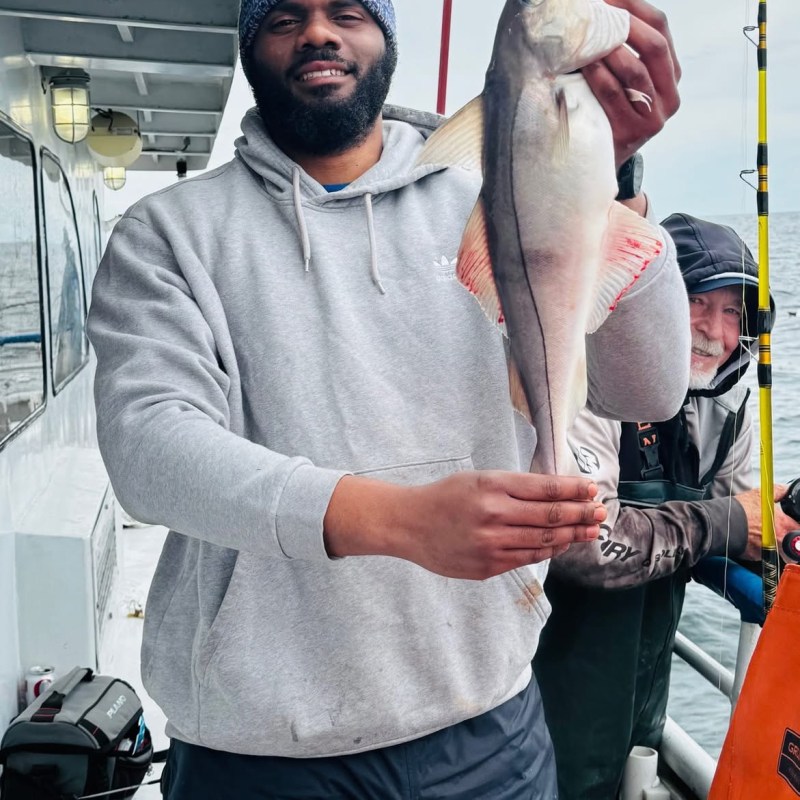 Person in a hoodie holding a large fish on a boat.