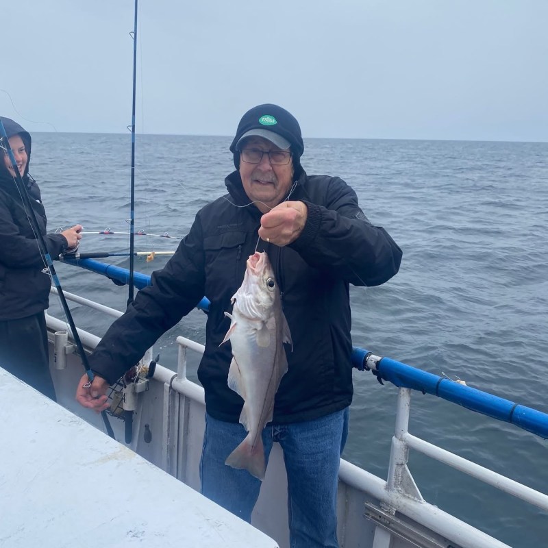 Person holding a fish on a boat with the ocean in the background.
