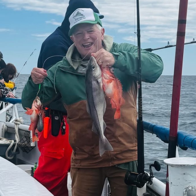 Person on boat holding two fish with fishing rod.