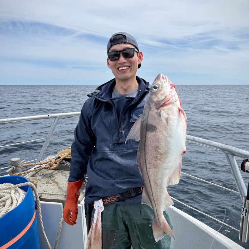 Person on a boat holding a large fish, smiling with ocean in the background.