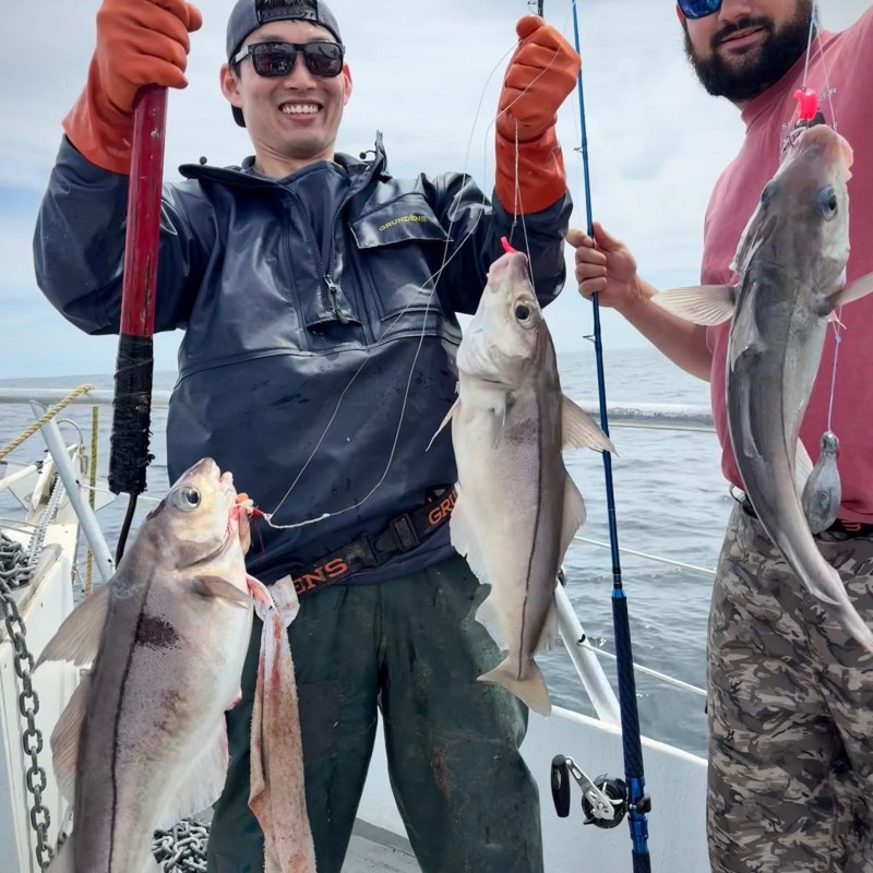 Two people on a boat holding fishing rods and caught fish.