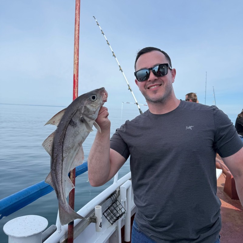 Man on boat holding a large fish, wearing sunglasses and a gray shirt.