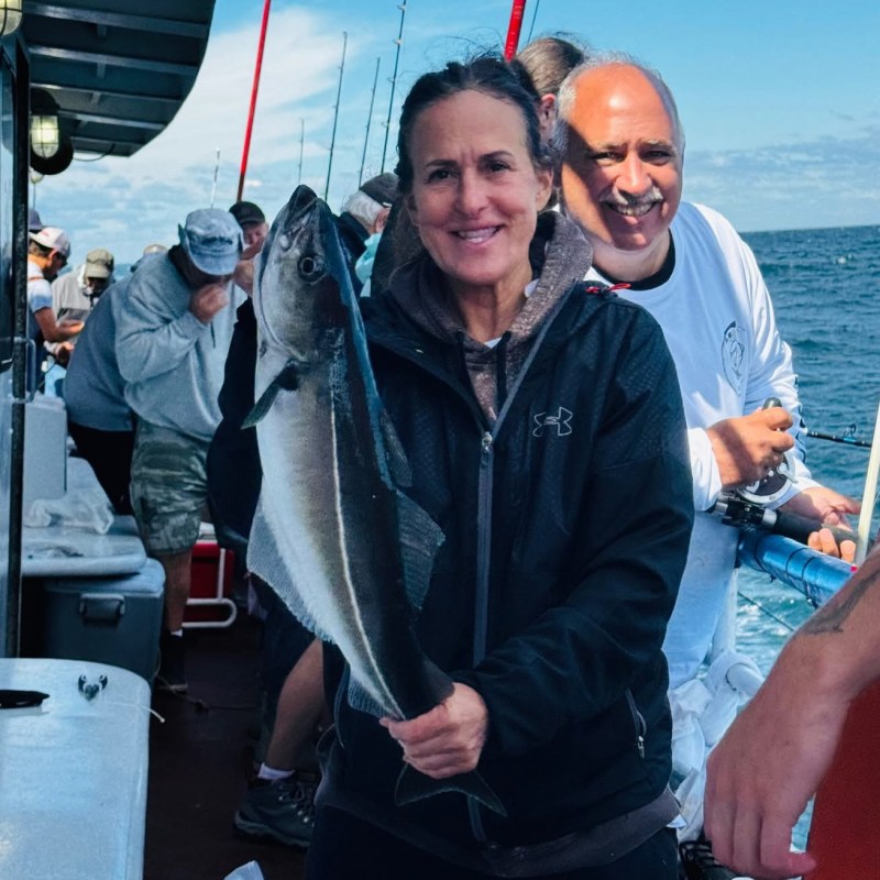 Person holding a large fish on a boat with people fishing in the background.