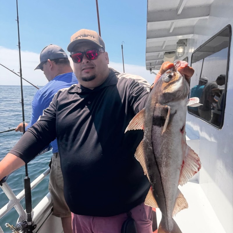 Man on boat holding a fish, another person in the background fishing.