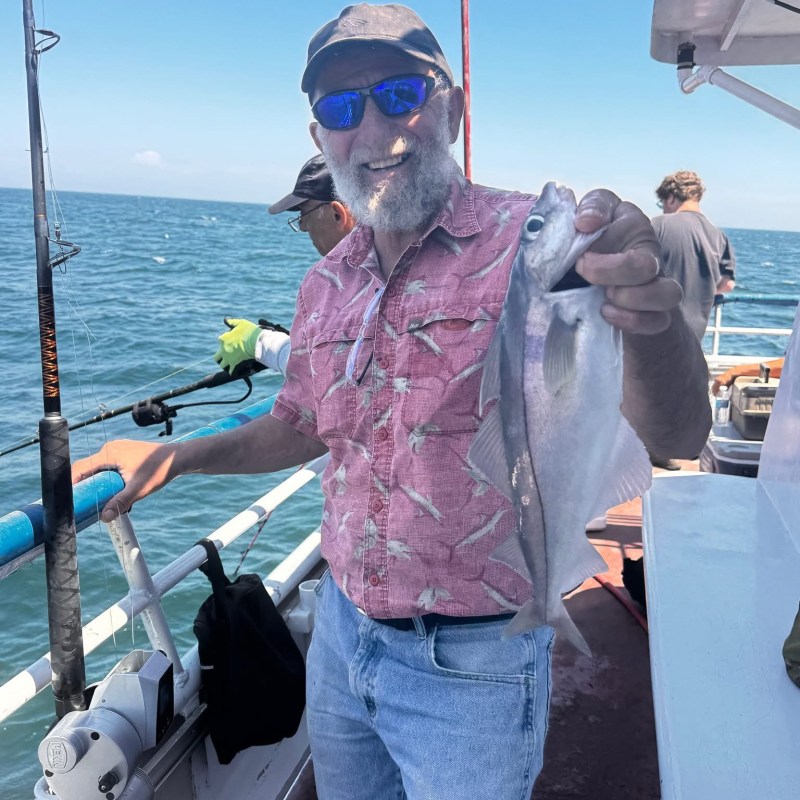 Man in sunglasses holding a fish on a boat with ocean in background.