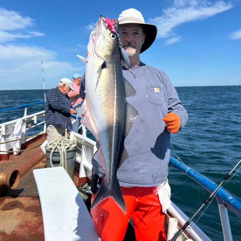 Man holding a large fish on a boat under a clear sky.