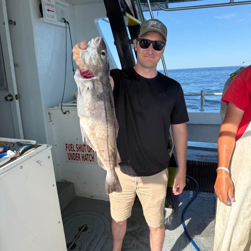 Person holding a fish on a boat next to another person.