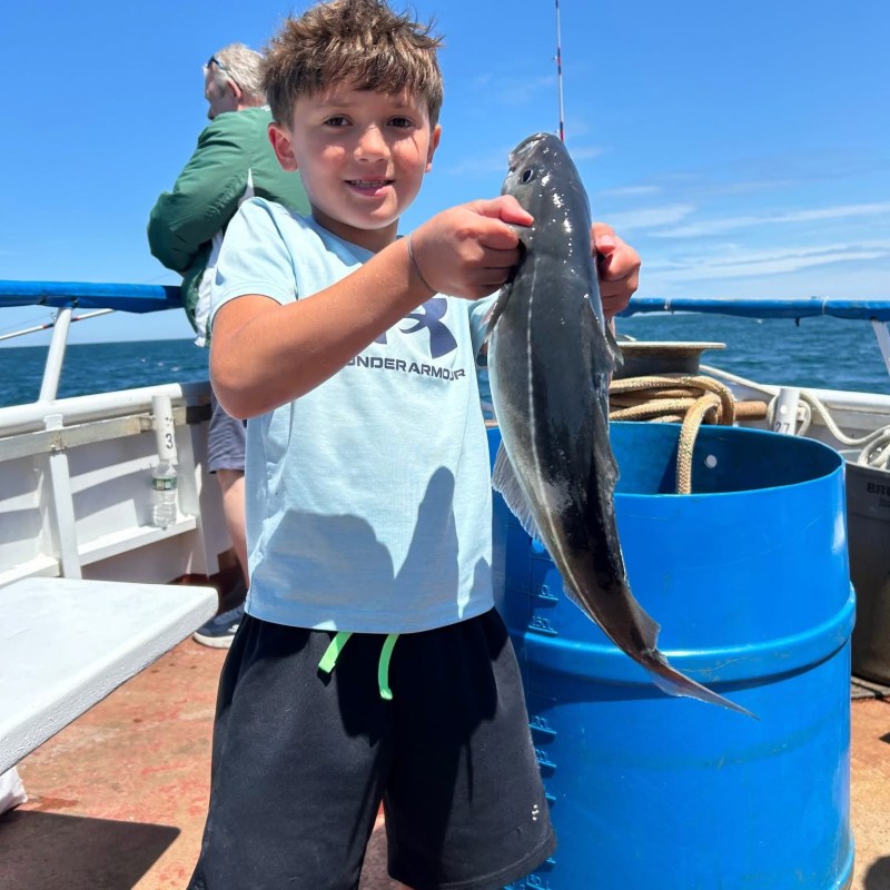 Smiling boy holding a fish on a boat.