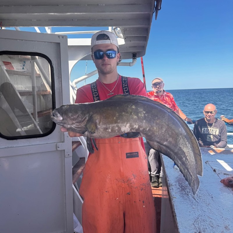 Person in orange overalls holding a large fish on a boat, with others seated in the background.