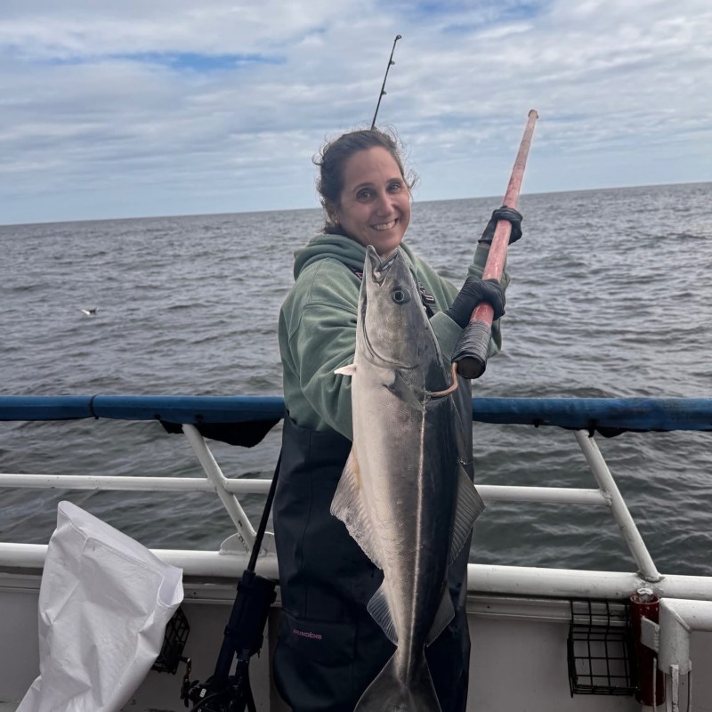 Person on boat holding a large fish, with ocean in background.