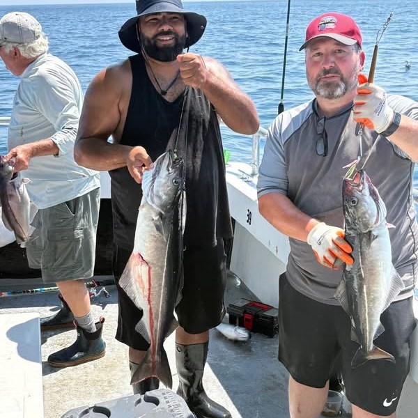 Two men on a boat holding large fish, smiling at the camera.