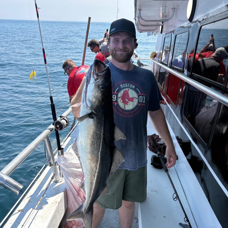 Man holding large fish on a boat with ocean background.