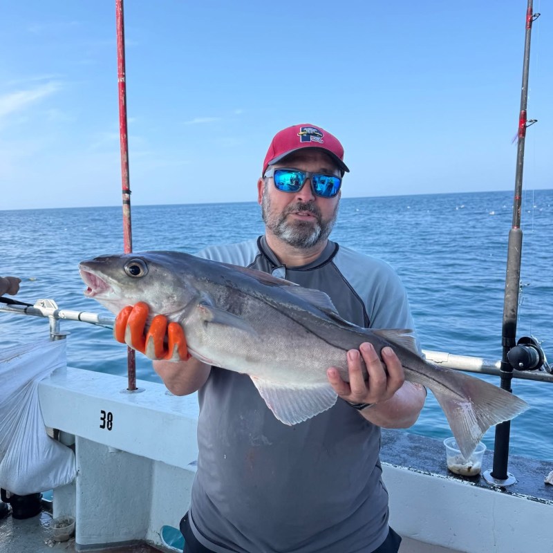 Man holding a large fish on a boat with fishing rods in view.