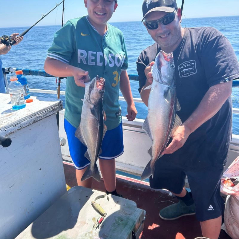 Two people on a boat holding freshly caught fish, smiling at the camera.