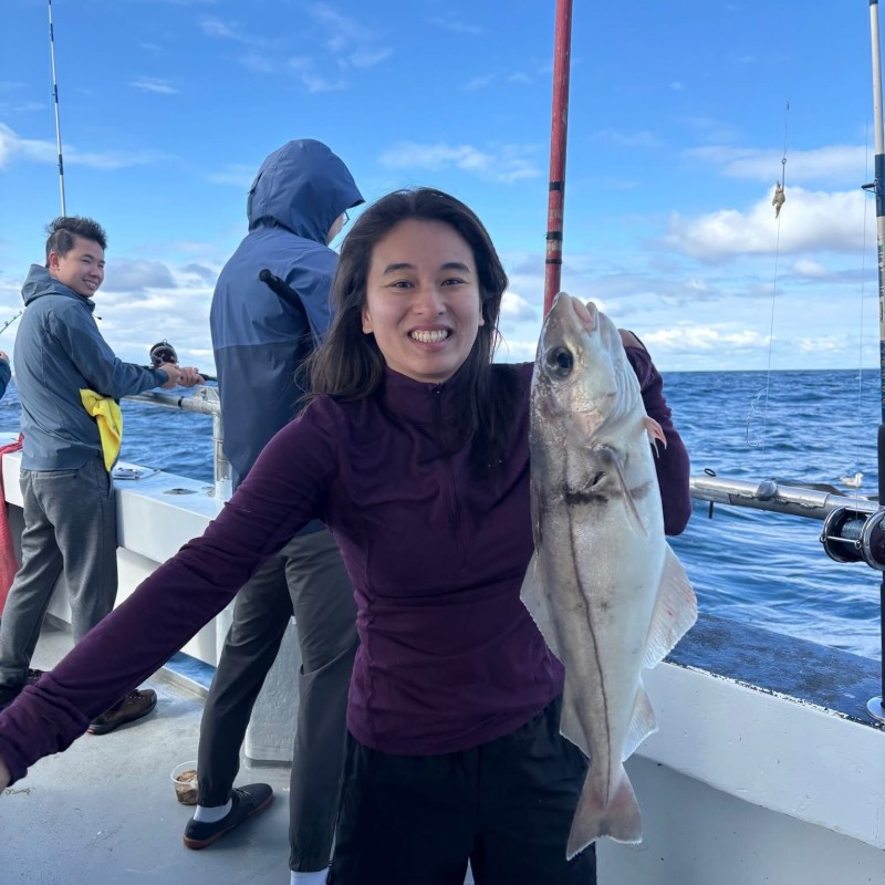 Person holding a large fish on a boat, with ocean and blue sky in the background.