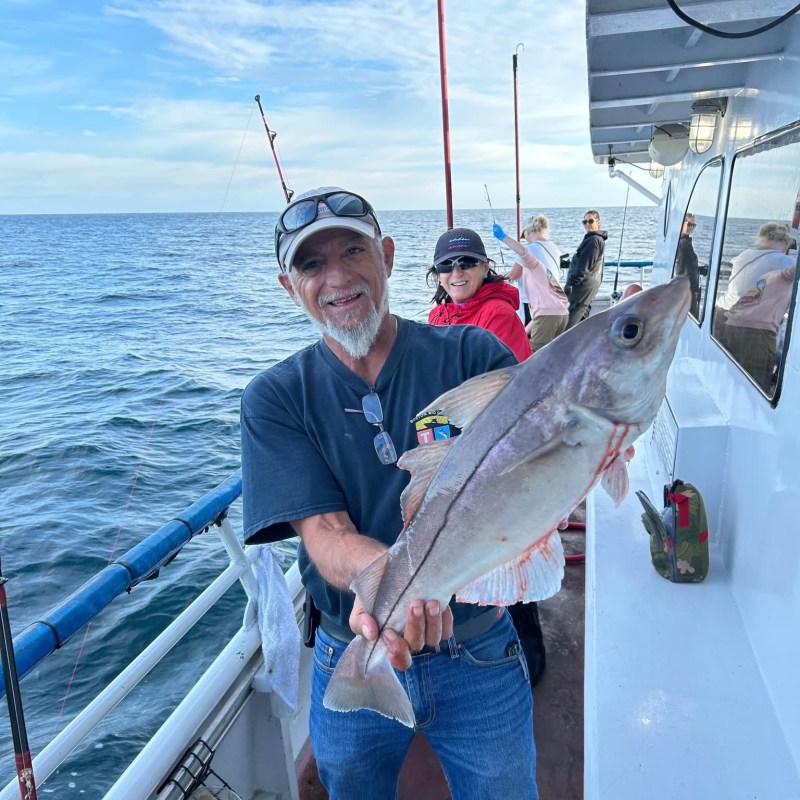 Man smiling on boat holding large fish, ocean background.